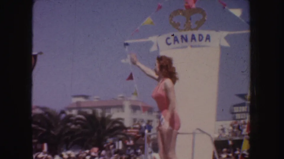 1952 California parade view of a contestant in a pink swimsuit waving near a tall white float marked Canada.