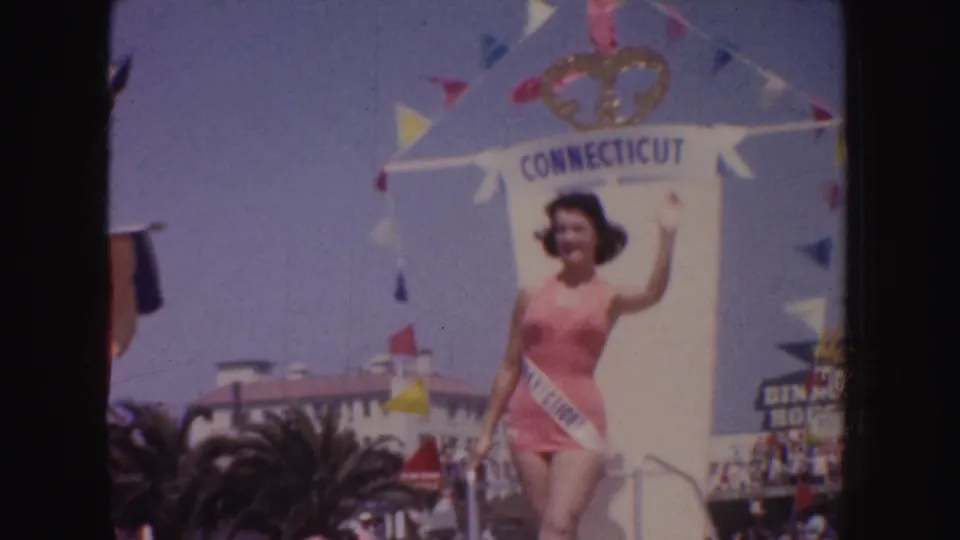 1952 California parade frame showing a smiling contestant in a pink swimsuit and sash on a float marked Connecticut.