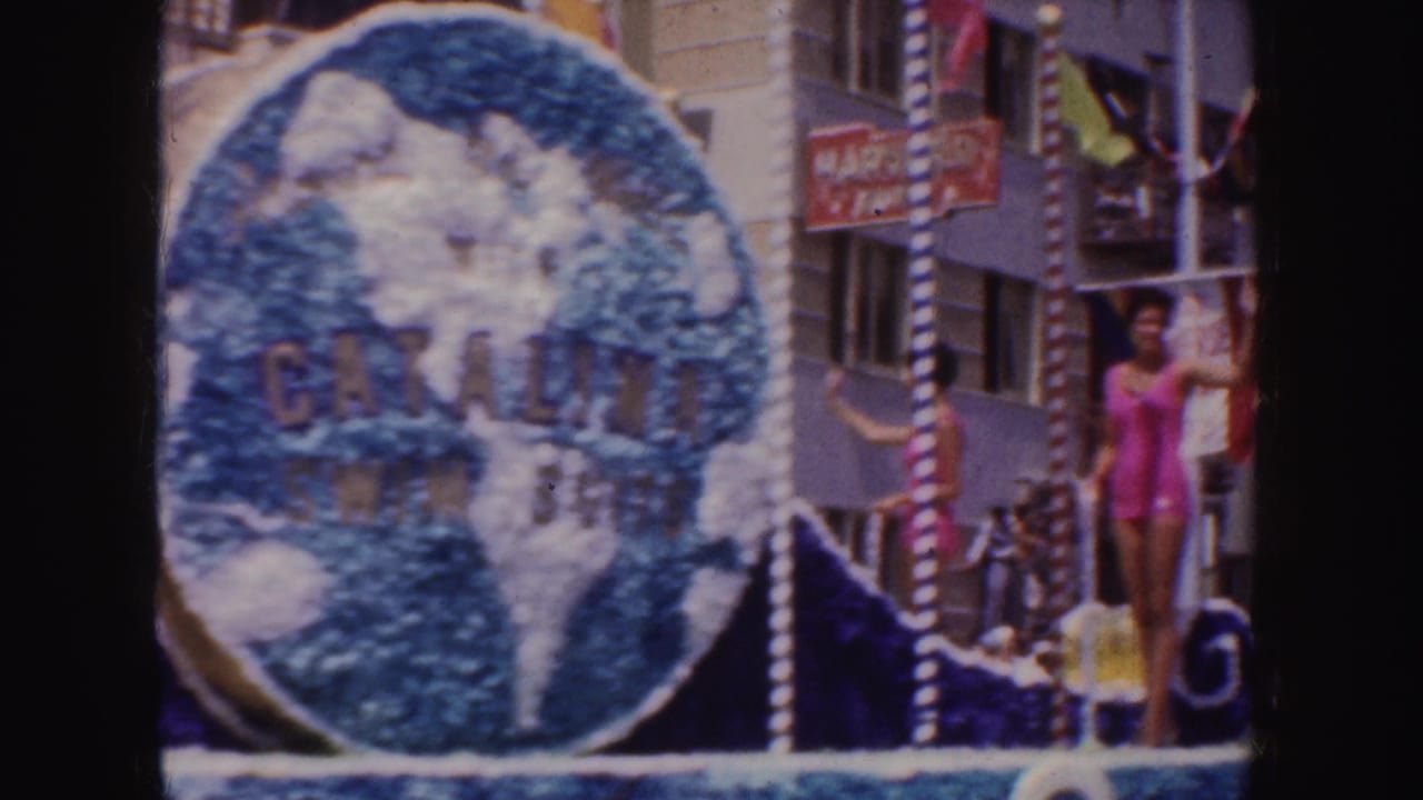1952 California parade frame showing a float with a large globe sign reading Catalina Swim Suit and a woman in a pink swimsuit waving.