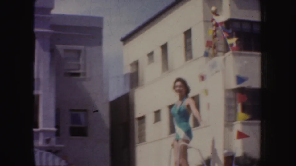 A beauty queen on a float waves during a 1952 California street parade, filmed in soft 8mm color.