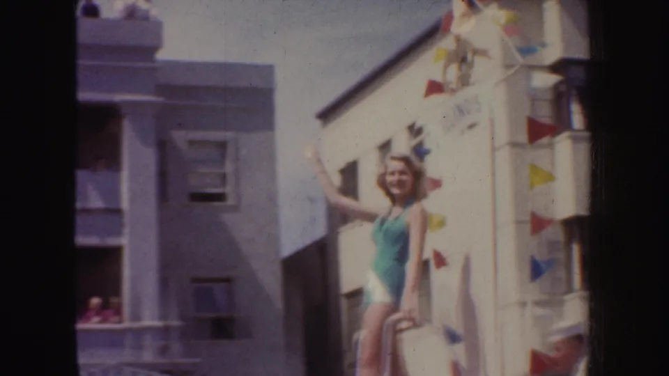 1952 California parade footage shows another view of the swimsuit-clad beauty queen waving beside bunting and balconies.