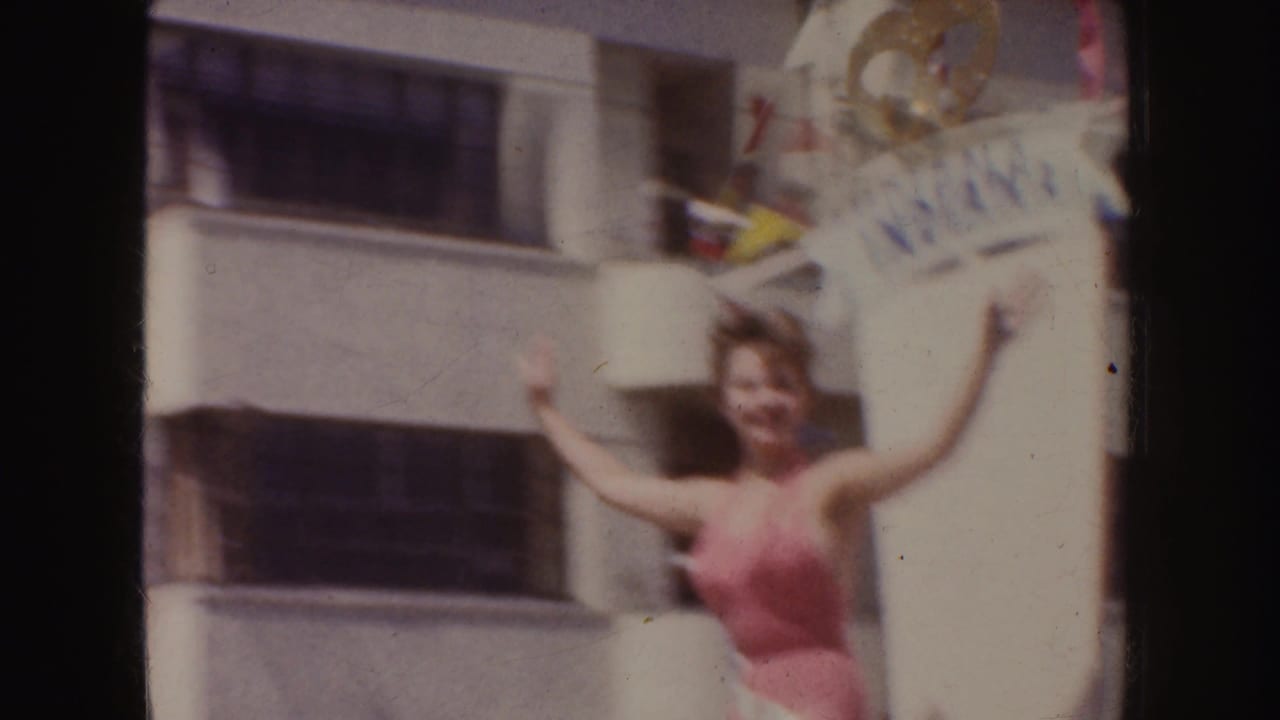 Woman in a pink swimsuit waves beside a float sign reading France.