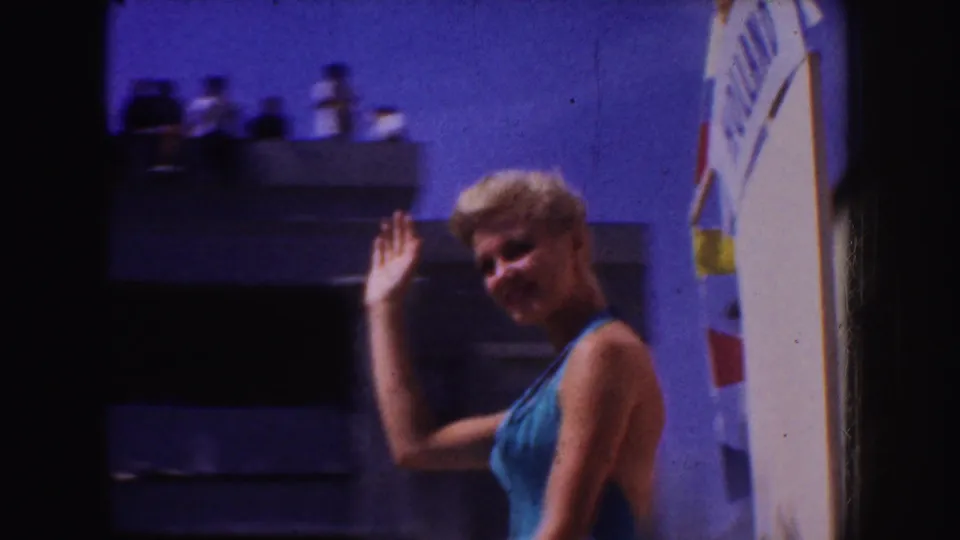 A closer 8mm view shows the blonde woman smiling and waving, with part of the HOLLAND banner and flags at the frame edge.