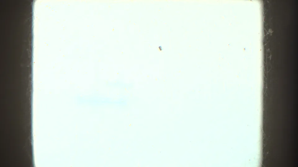 Overexposed 8mm frame with very little visible detail, bordered by dark film edges and small surface marks.