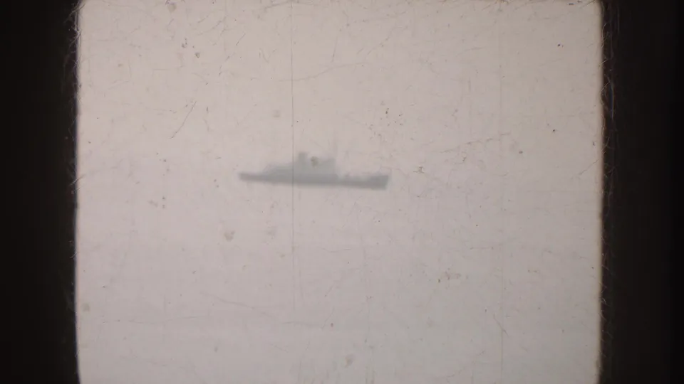 A distant gray vessel, possibly naval, is silhouetted on hazy California water with scratches and soft 8mm texture.