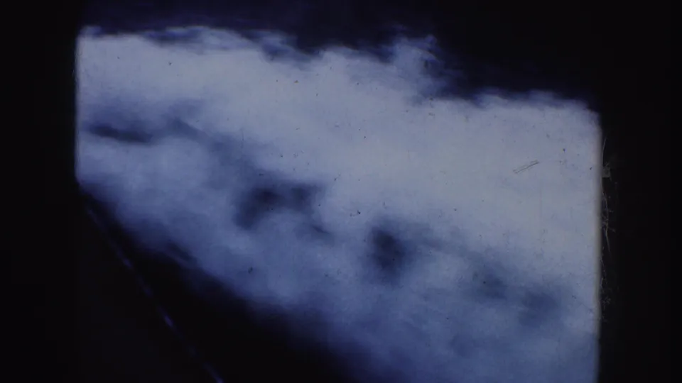 Handheld 8mm view of blue-white motion, possibly water or wake, with a diagonal dark line and visible film texture.