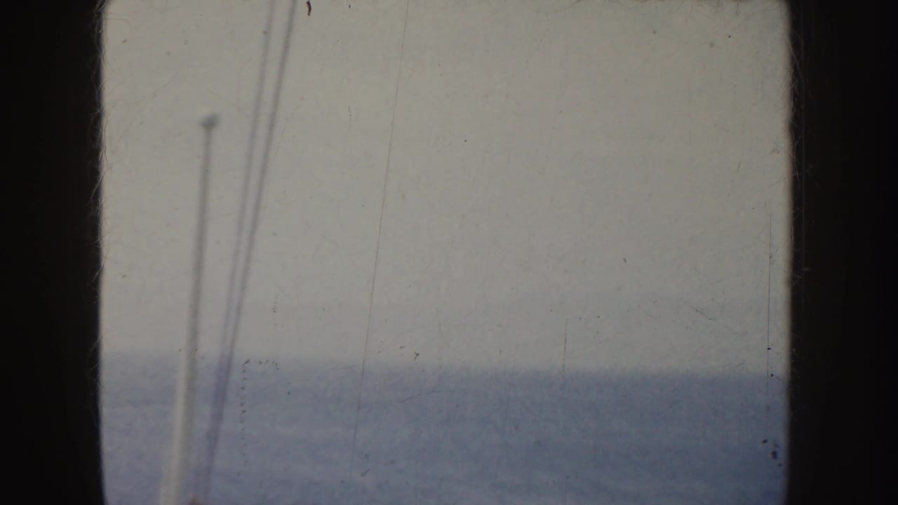1952 California 8mm frame showing a hazy ocean horizon, overcast sky, and pale vertical rigging near the left edge.