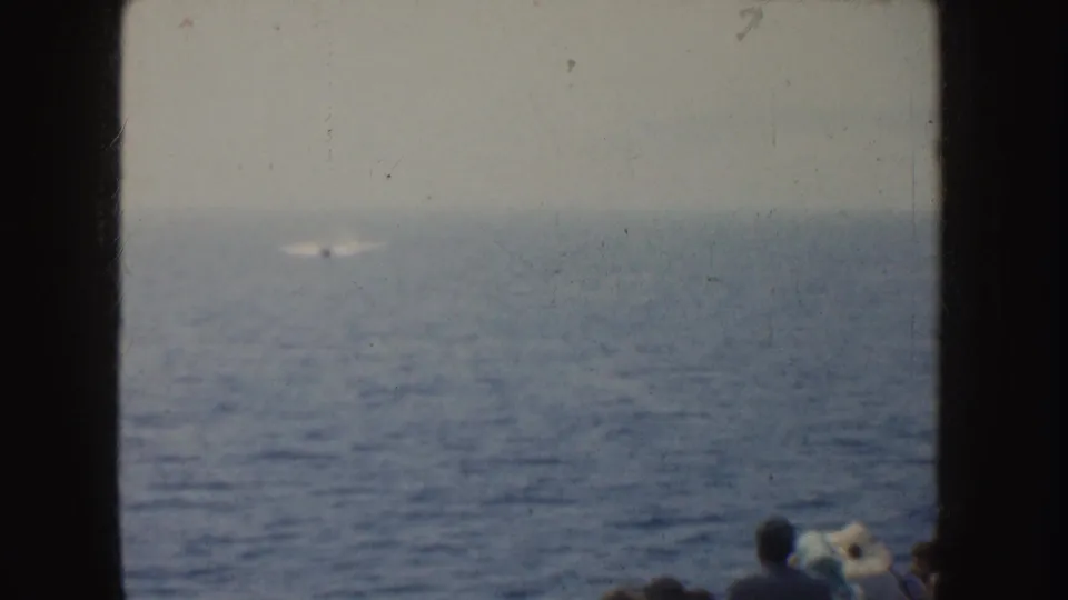 1952 California 8mm frame showing a small white object on the ocean and partial silhouettes of people watching at lower right.