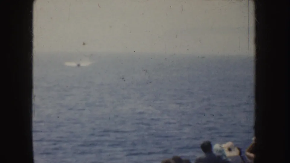 A small motorboat moves across distant California water in a soft 1952 8mm home-movie view, with onlookers partly visible below.