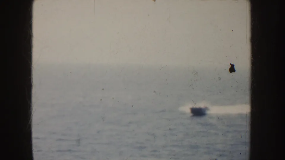 A small motorboat appears more clearly on the California sea in this 1952 8mm frame, trailing a bright wake across hazy water.