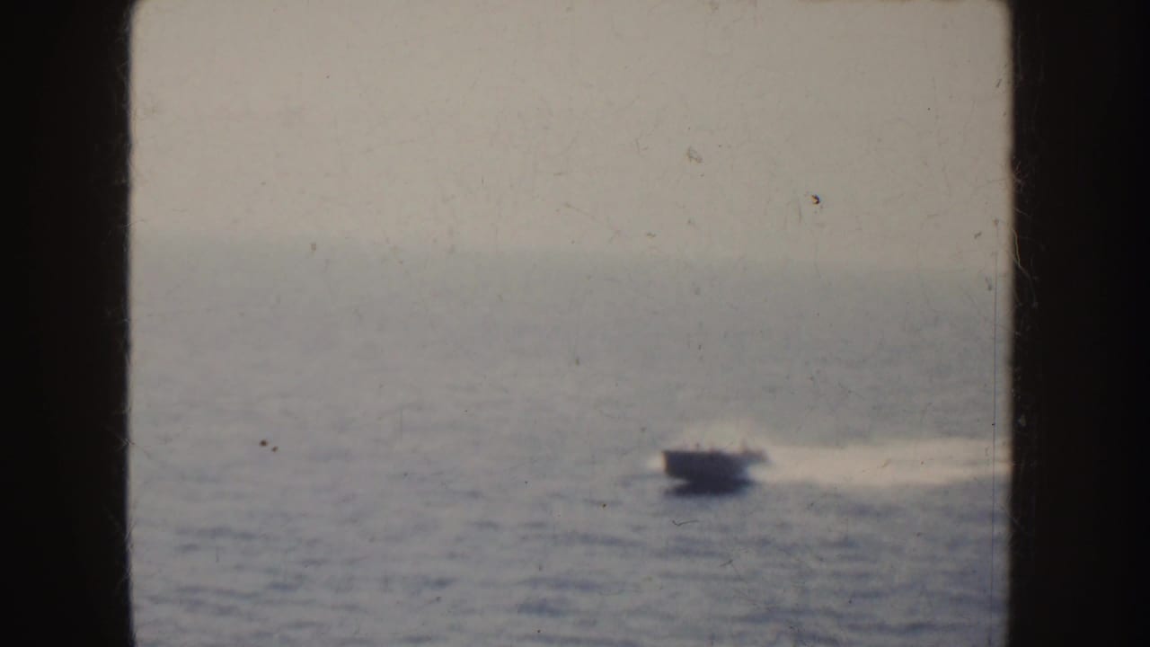 1952 California home-movie frame showing a small motorboat crossing the ocean with a pale wake and distant land on the horizon.