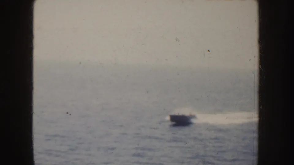 1952 California home-movie frame showing a small motorboat crossing the ocean with a pale wake and distant land on the horizon.