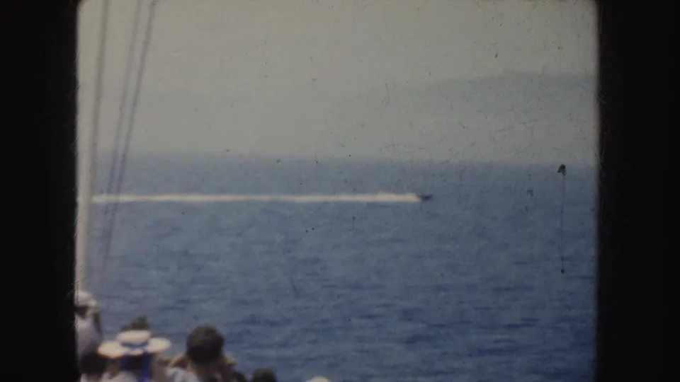 Shipboard 8mm frame from 1952 California footage, with passengers at the lower edge and a motorboat wake stretching across the sea.