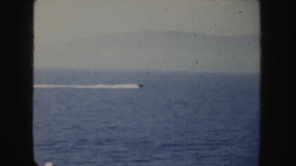 1952 California coastal home-movie view of a small motorboat receding across open water with a long white wake behind it.