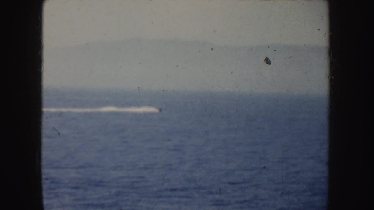 Distant speedboat wake crossing open water within dark film borders.