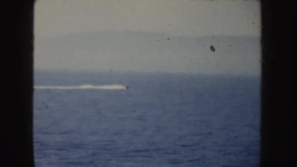 A distant fast boat or wake moves across open water in 1952 California 8mm home-movie footage.