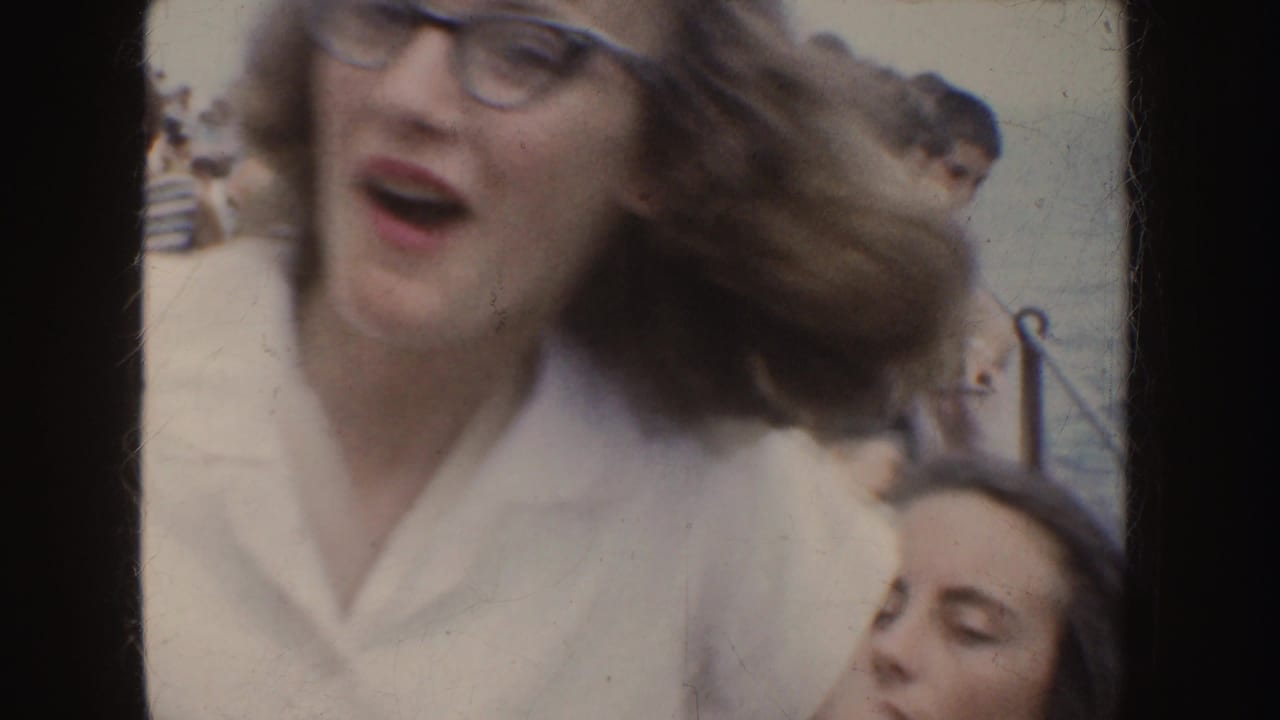 Woman in cat-eye glasses and a white shirt reacts close to the camera outdoors.