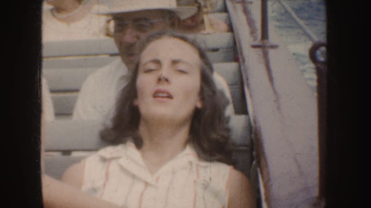 Young woman sits on a boat with eyes closed while a man in a white hat is partly visible behind her.