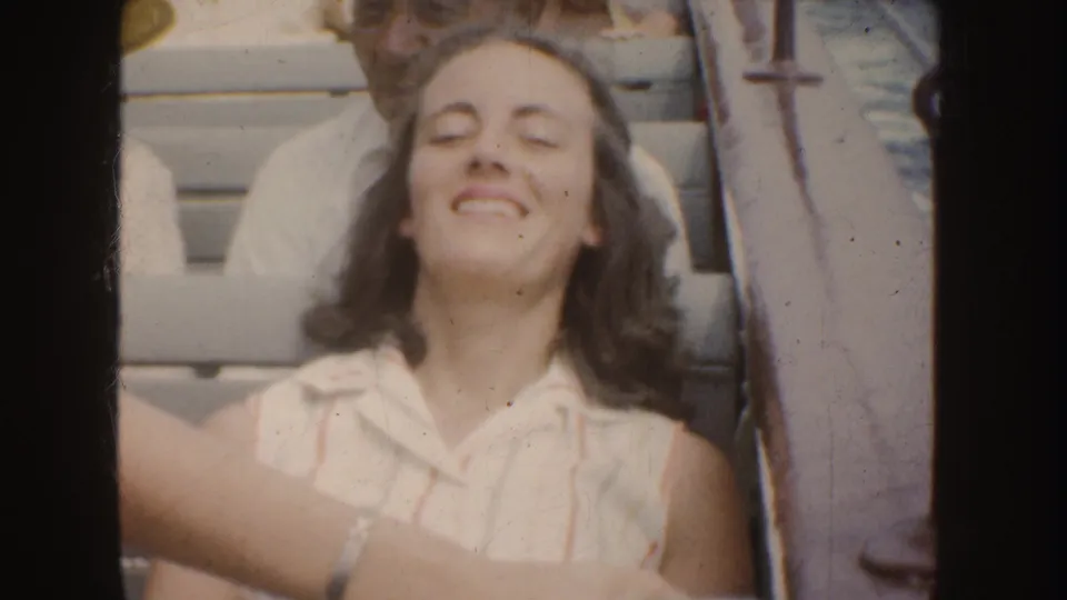 In supported 1952 California footage, the woman smiles broadly with eyes closed while seated on a boat in bright daylight.