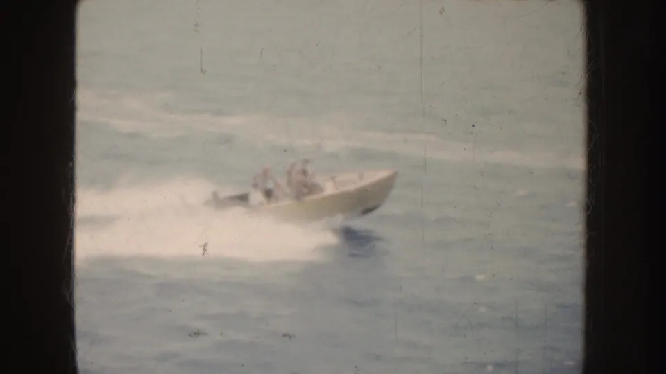 Cream speedboat carrying several passengers crests ocean waves in 1952 California 8mm footage, with spray and soft film texture.