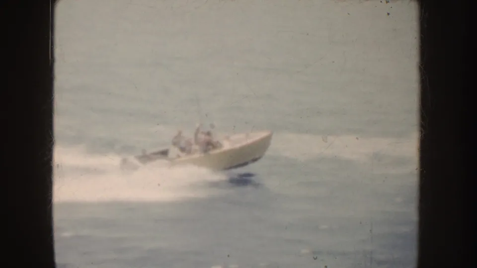 A cream speedboat with passengers cuts through California ocean waves, captured in soft 1952 8mm home-movie color.