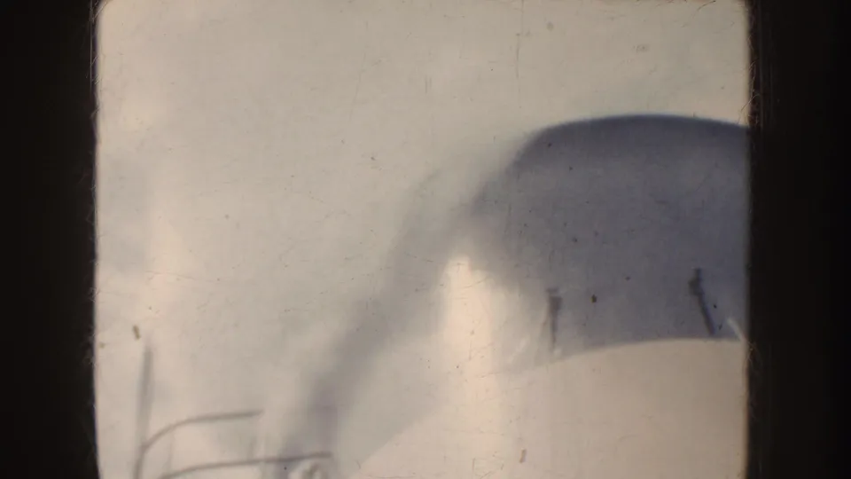 1952 California 8mm frame showing a rounded foreground structure seen through dark framing, with water and misty mountains beyond.