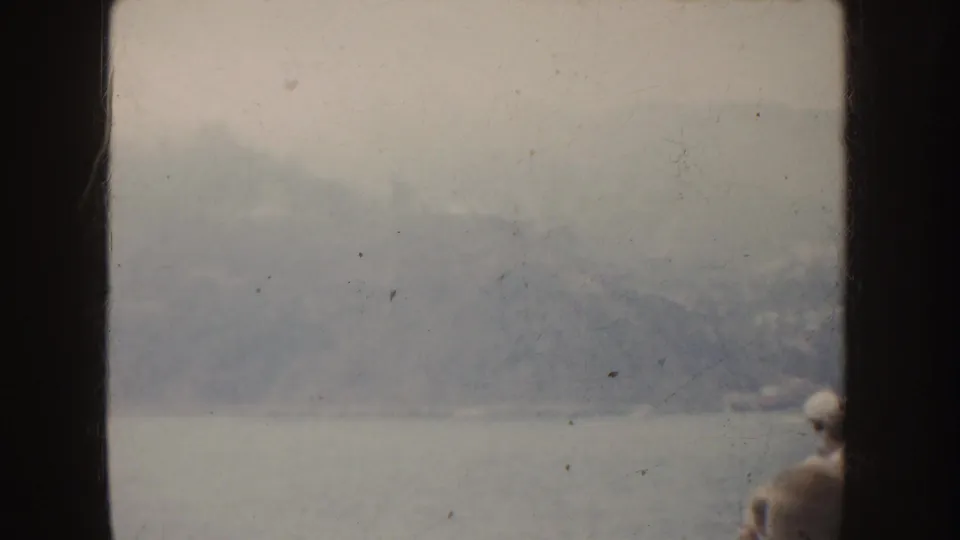 1952 California travel frame with misty mountains across water, dark window-like bars, and a small person partly visible at right.