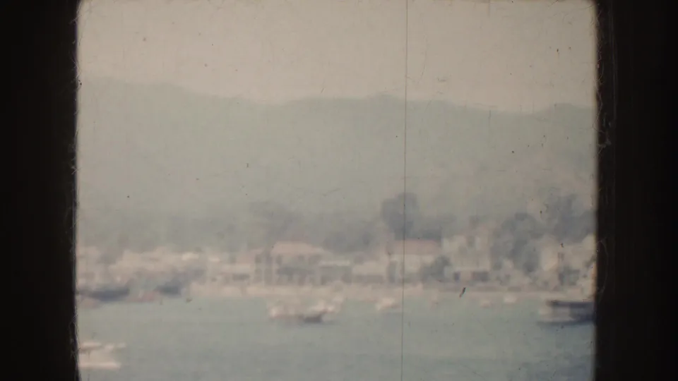 1952 California frame showing distant shoreline buildings and boats across water, backed by misty mountains.