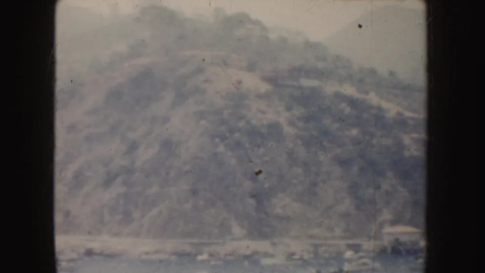 Soft 8mm frame showing a California harbor edge below a steep hillside, with boats and shoreline structures partly visible.
