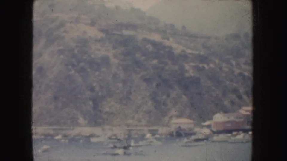 Faded 1952 California home-movie frame showing small boats near shore with a wooded hillside rising behind them.