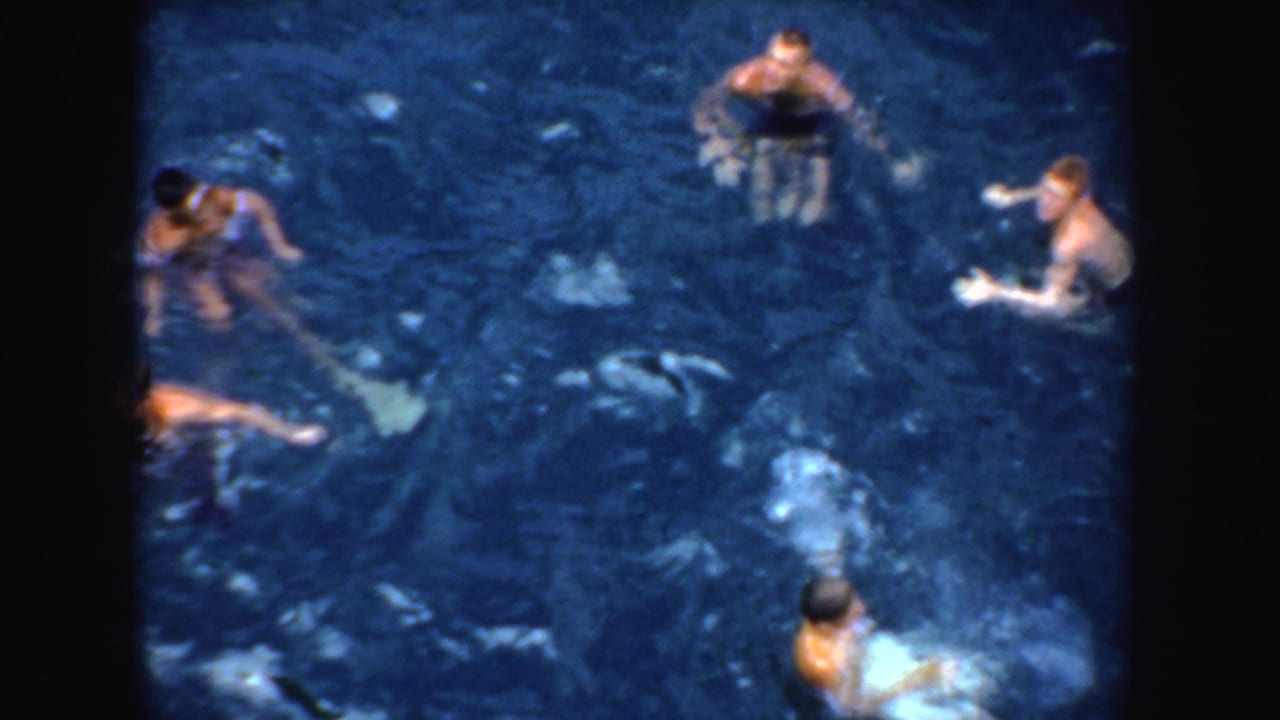 1952 California home-movie frame showing several people in swimwear treading water in dark blue water from an elevated viewpoint.