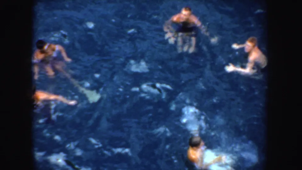 1952 California home-movie frame showing several people in swimwear treading water in dark blue water from an elevated viewpoint.