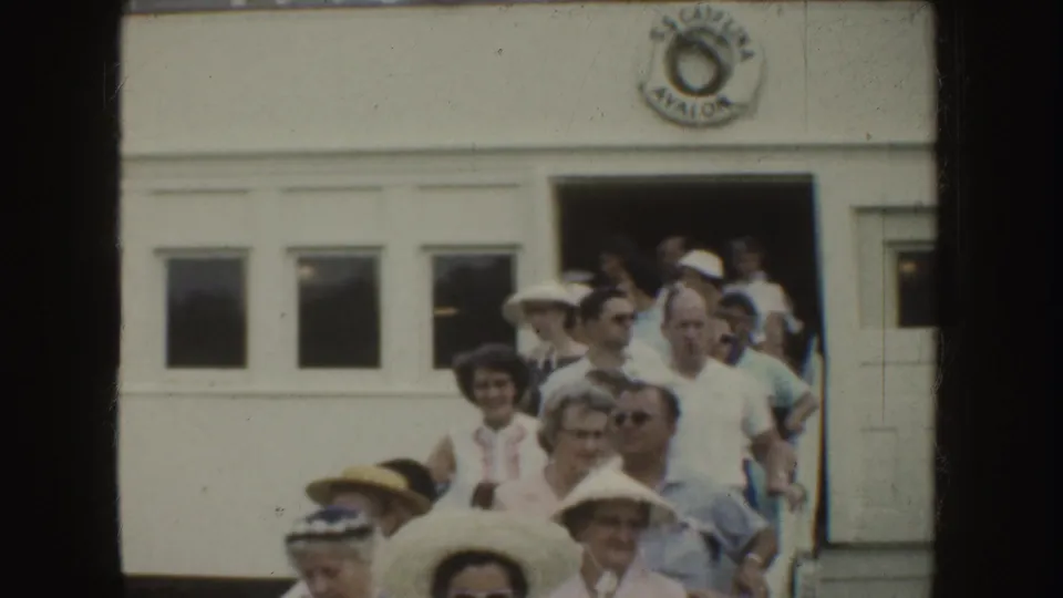 1952 California home-movie frame showing adults in hats and light shirts leaving a white bus with a circular side logo.