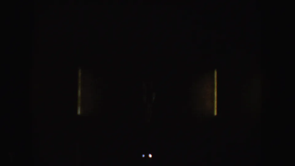 Underexposed 8mm frame from the bus scene with only faint light marks and small bright spots visible.