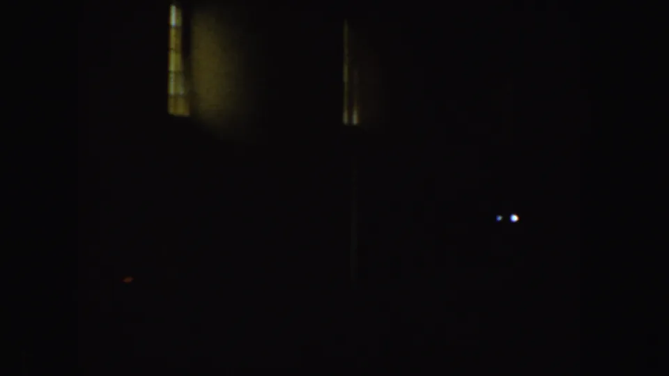 Nearly black 8mm frame from the clip, showing small bright dots and faint vertical highlights but little identifiable subject matter.