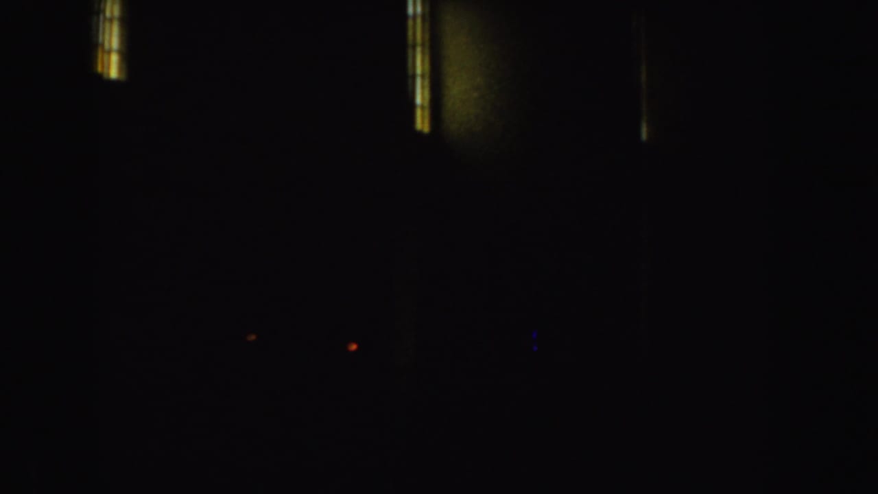 Dark opening frame from 1952 8mm footage, with small vertical window lights visible before the outdoor scene.