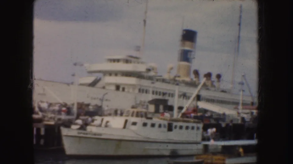 The 1952 harbor scene shows a white passenger ship, dockside crowding, and a small boat moored in the foreground.