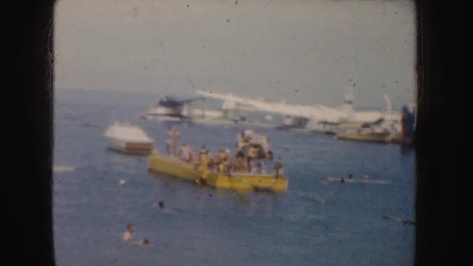 1952 California harbor view with people gathered on a yellow floating platform, swimmers in the water, and boats in the background.