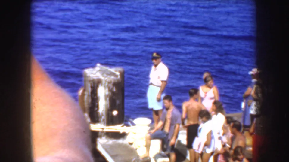1952 California home-movie frame showing people gathered near a waterfront dock with deep blue water behind them.