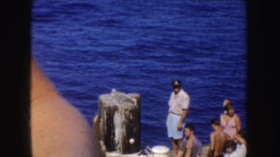 1952 California frame with waterfront visitors near weathered posts, viewed through dark film gate edges.