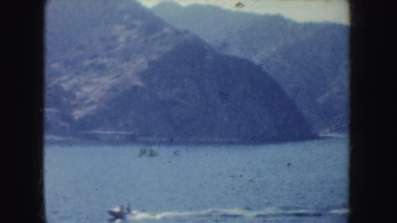 1952 California home-movie view from the water toward a hazy mountainous shoreline, with small-gauge film edges visible.