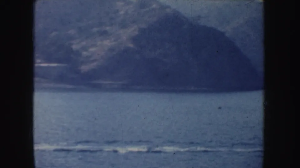 A small powerboat speeds over calm water near a hazy California mountain shoreline, with wake visible in the foreground.