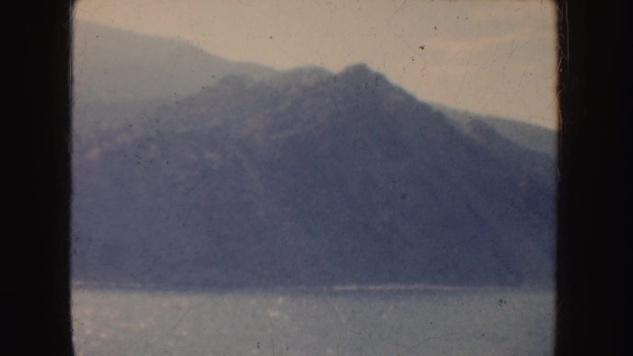 1952 California 8mm frame showing blue-gray mountains beyond calm water, with soft focus, dust and dark gate edges.