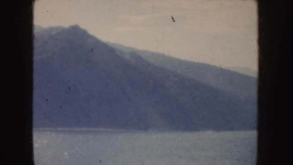 Soft 8mm view of a California mountain shoreline across water, tinted blue-purple and marked by fine scratches.