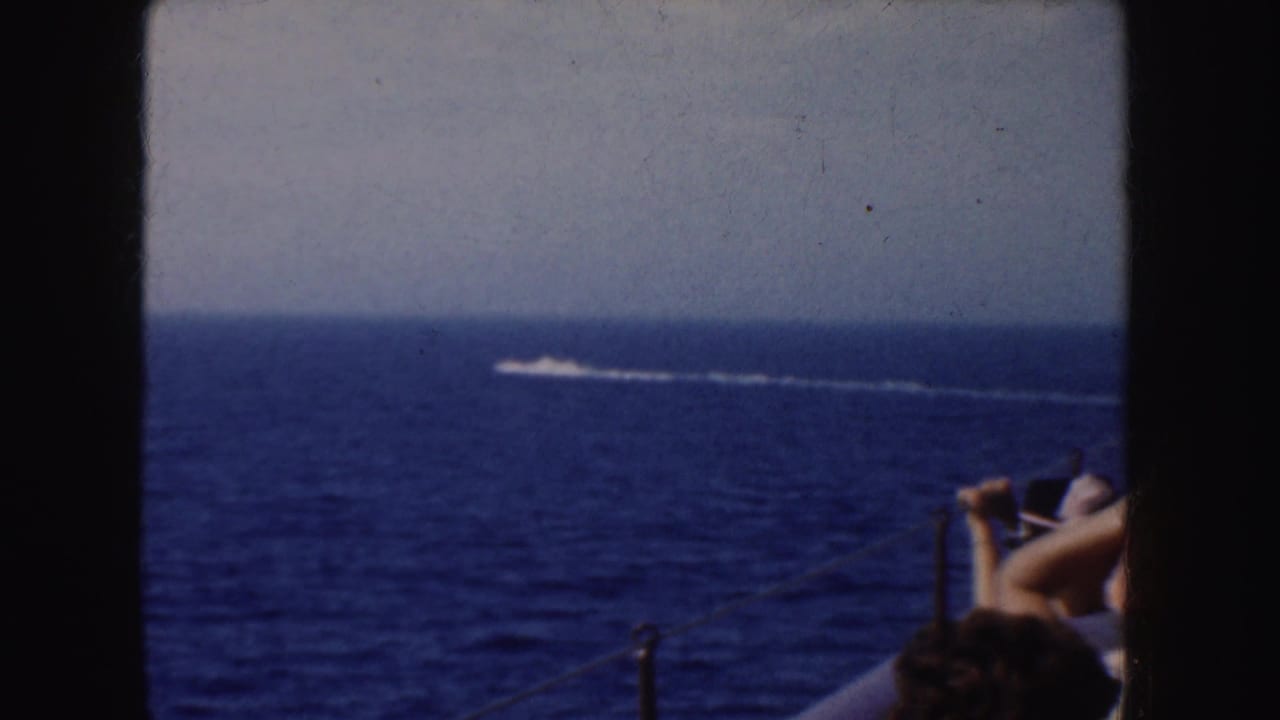 1952 California 8mm frame showing blue ocean, pale sky, a distant white wake, boat railing, and partial passengers in the foreground.