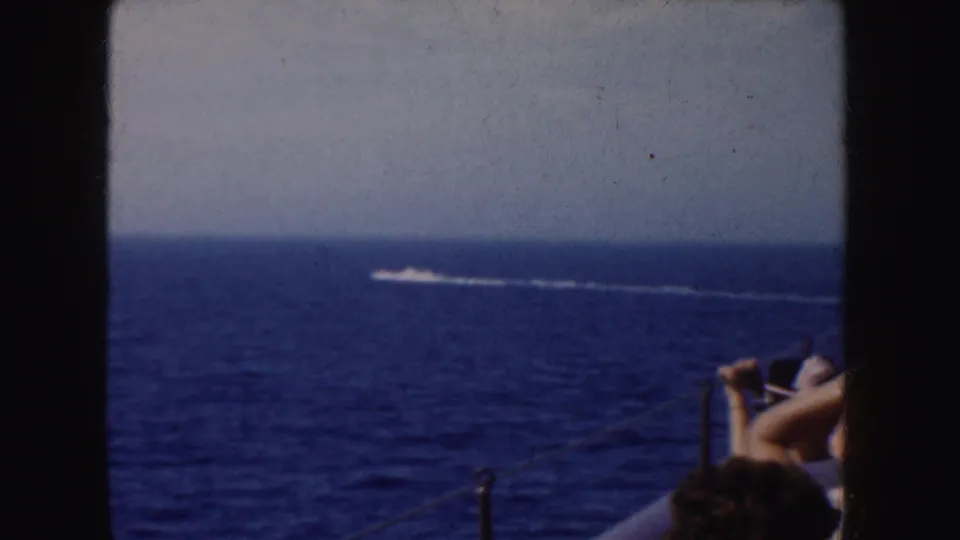 1952 California 8mm frame showing blue ocean, pale sky, a distant white wake, boat railing, and partial passengers in the foreground.