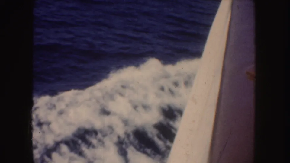 1952 California boating frame showing foamy water alongside the vessel, a slanted boat edge, open ocean, and a distant white wake.
