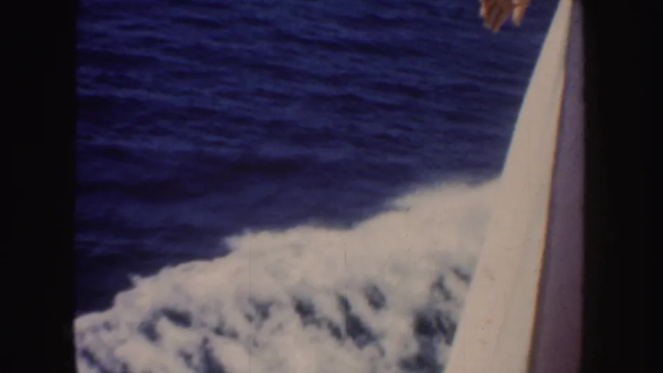 1952 California 8mm frame of ocean wake beside a white boat edge, with only a partial hand visible at the top edge.