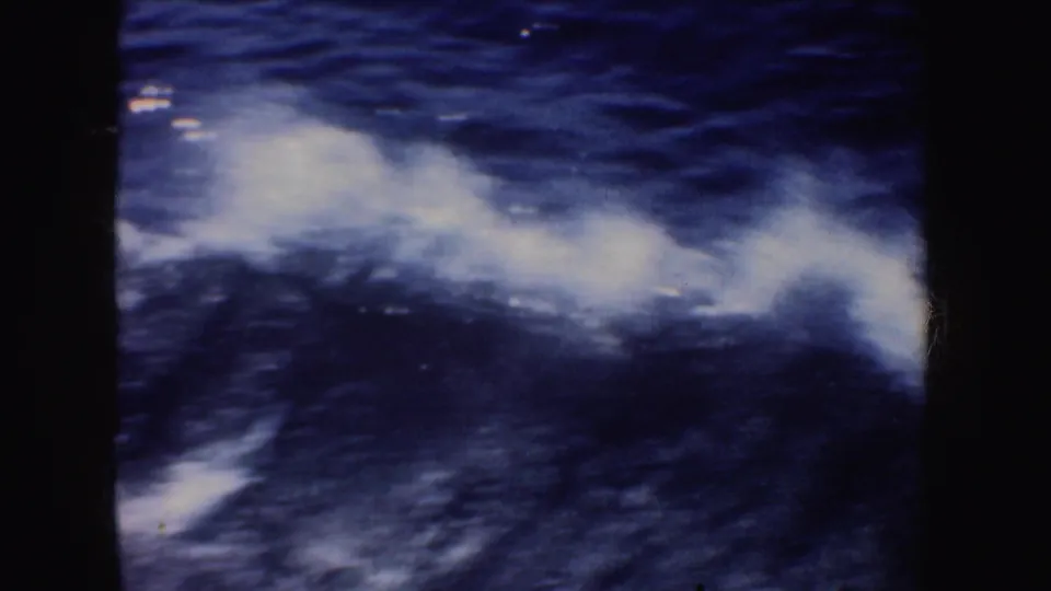 A 1950s 8mm boating view of white sea spray stretching across dark blue water, framed by black film edges.