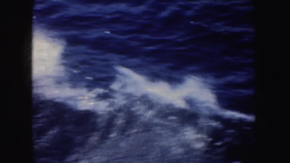 Close 8mm home-movie view of churning white wake and blue water during a California boat ride.